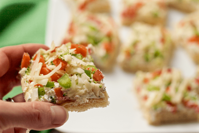 A hand picking up a cold veggie pizza square