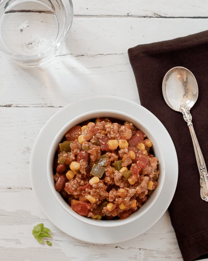 A ground turkey stew with beans, corn and veggies in a bowl with a brown napkin and spoon to the side.