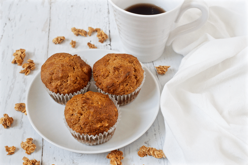 A small white plate with three muffins and a cup of coffee in the background.