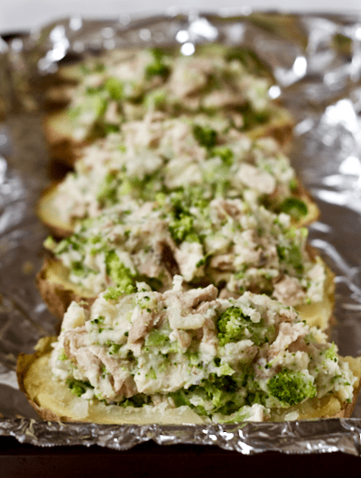 Four baked potato halves stuffed with a chicken and broccoli mixture on a foil lined baking sheet before being baked again.