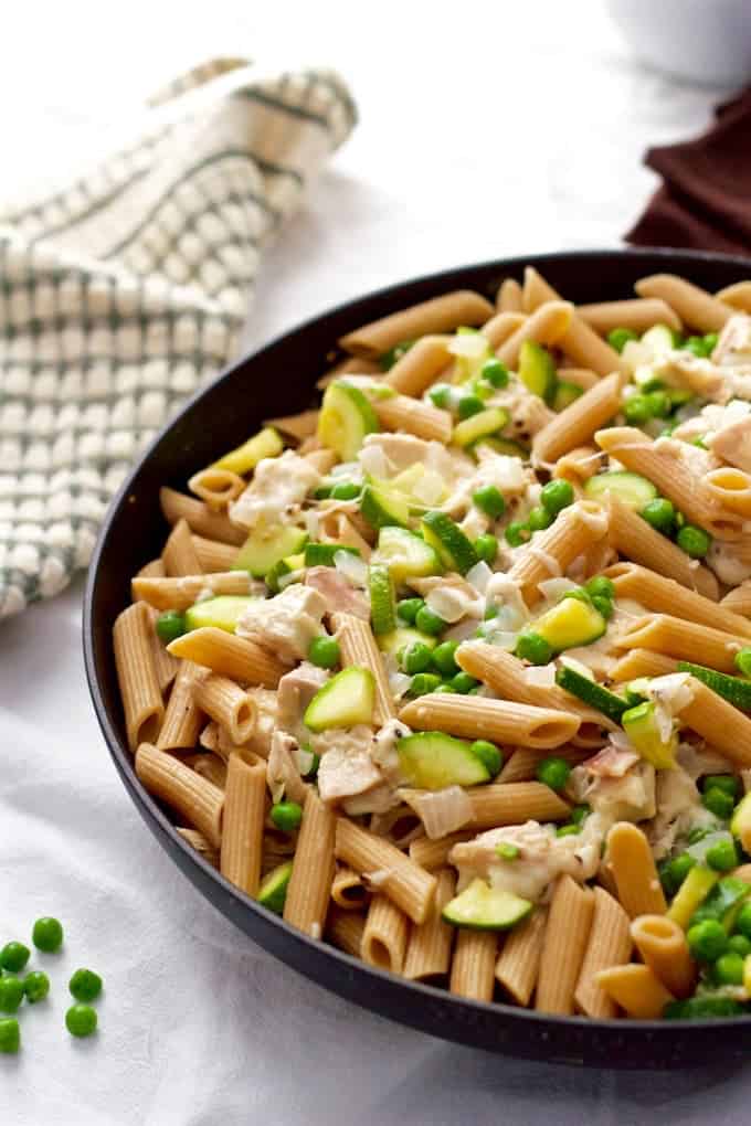 Cheesy pasta with rotisserie chicken, zucchini and peas is a 20-minute dinner the whole family will love! #chickenpasta #chickendinner #easyrecipes A large skillet full of a cheesy chicken pasta with zucchini and peas.