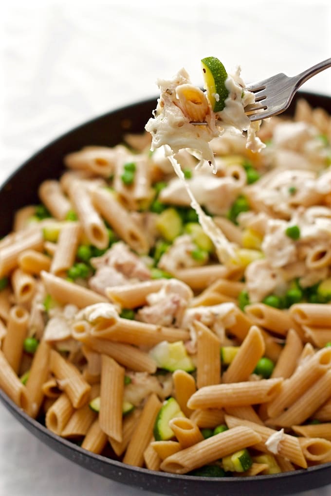 A fork getting a bite of a cheesy chicken pasta with zucchini and peas from a large skillet.