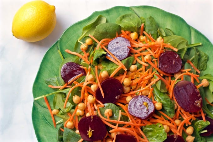 A spinach and beet salad with chickpeas and carrots with a lemon to the side.