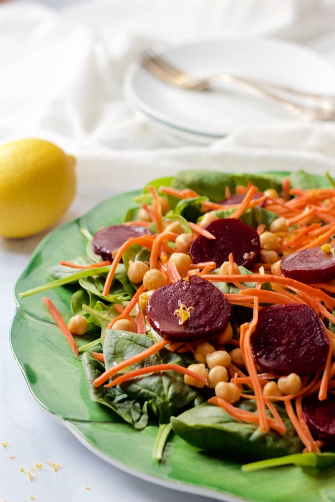 Close up of a spinach and beet salad with chickpeas and carrots with a lemon to the side.