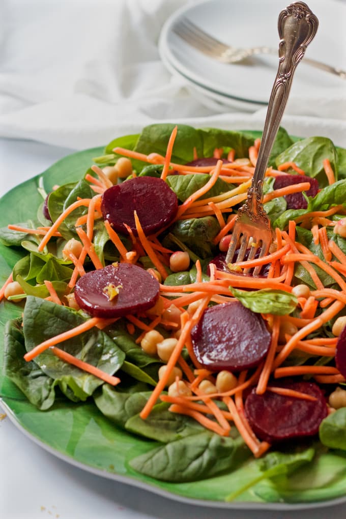 A fork getting a bite a spinach and beet salad with chickpeas and carrots.