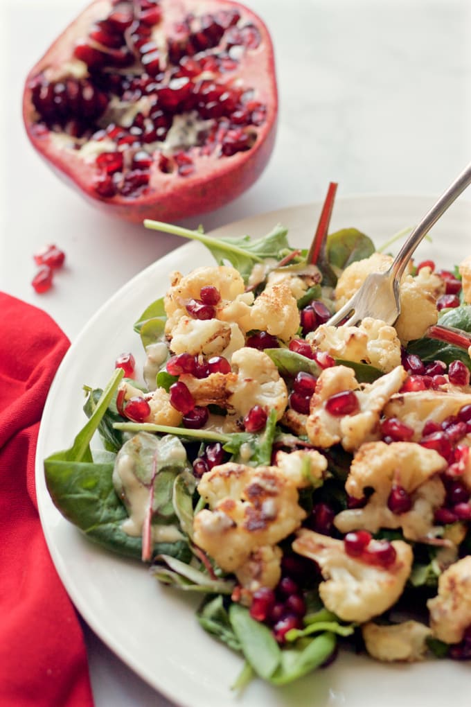 Baby kale and roasted cauliflower salad sprinkled with pomegranate seeds and drizzled with a creamy tahini dressing | FamilyFoodontheTable.com