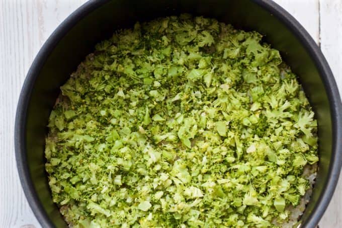 Chopped broccoli added to a pot of steamed brown rice before being mixed in.