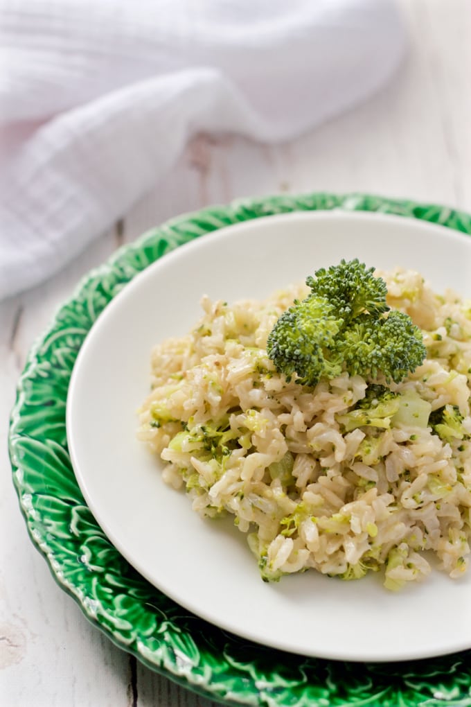 Broccoli cheese rice served on a white plate with broccoli for a garnish