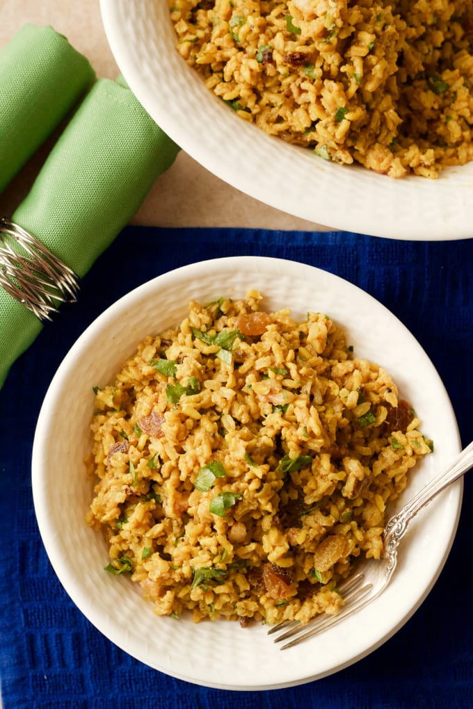 Curried brown rice with raisins and parsley served in a white bowl with a fork tucked in