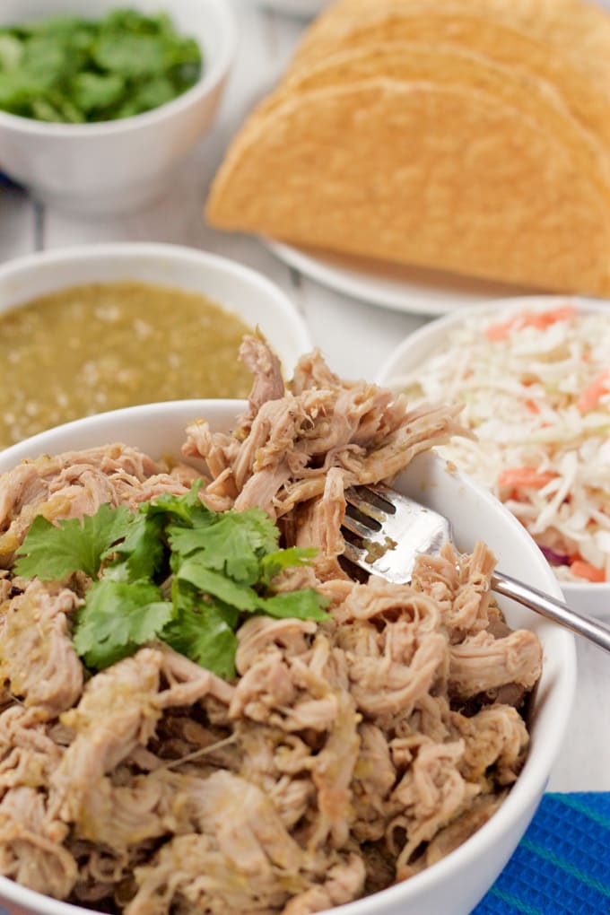 A forkful of crock pot salsa verde shredded pork being taken from a bowl