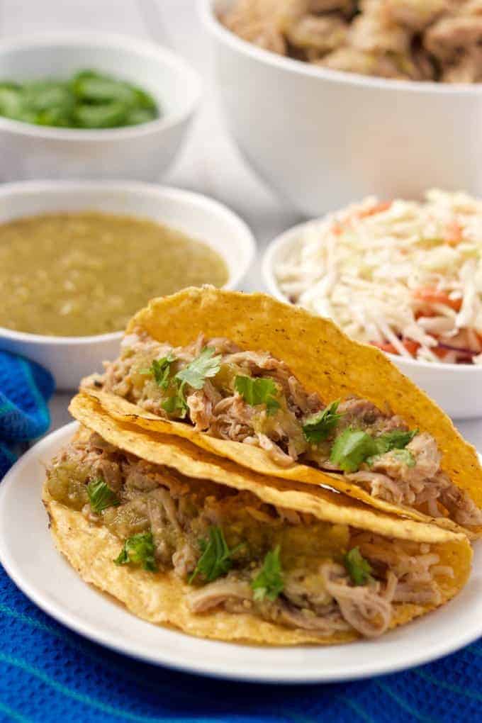 Slow cooker salsa verde shredded pork piled into some tacos with toppings in the background