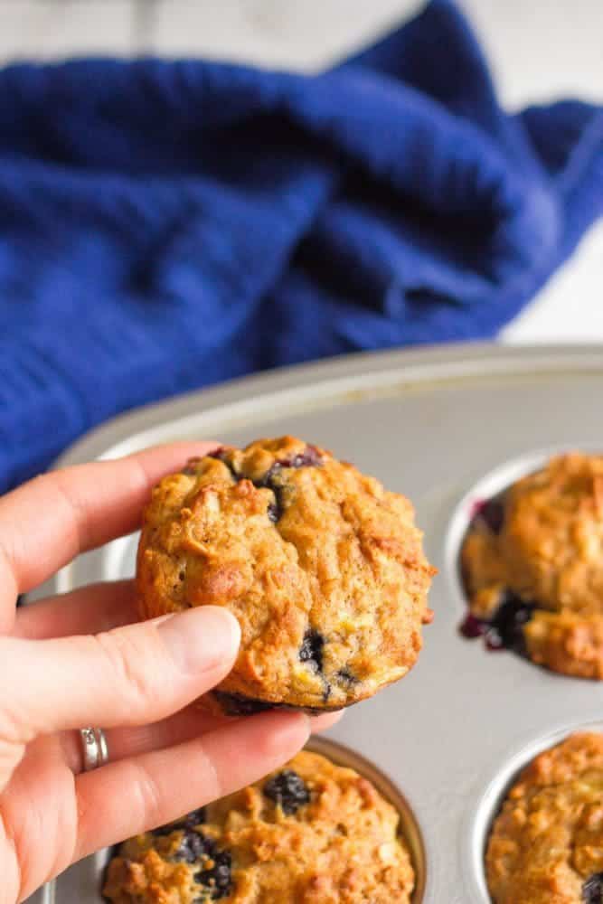 A hand picking up a banana blueberry muffin from a muffin tin