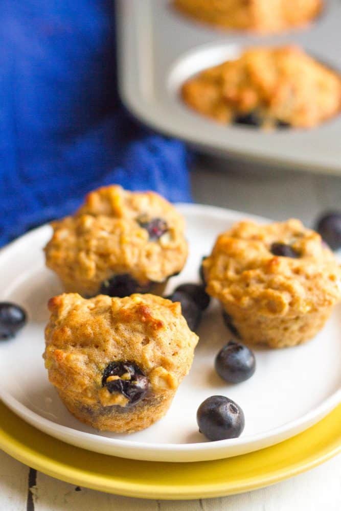 Mini whole grain blueberry muffins on a plate with extra blueberries scattered around