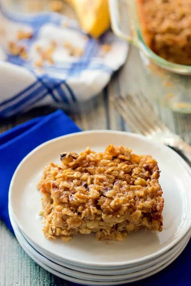 A piece of banana bread baked oatmeal being served on a white plate with the pan in the background