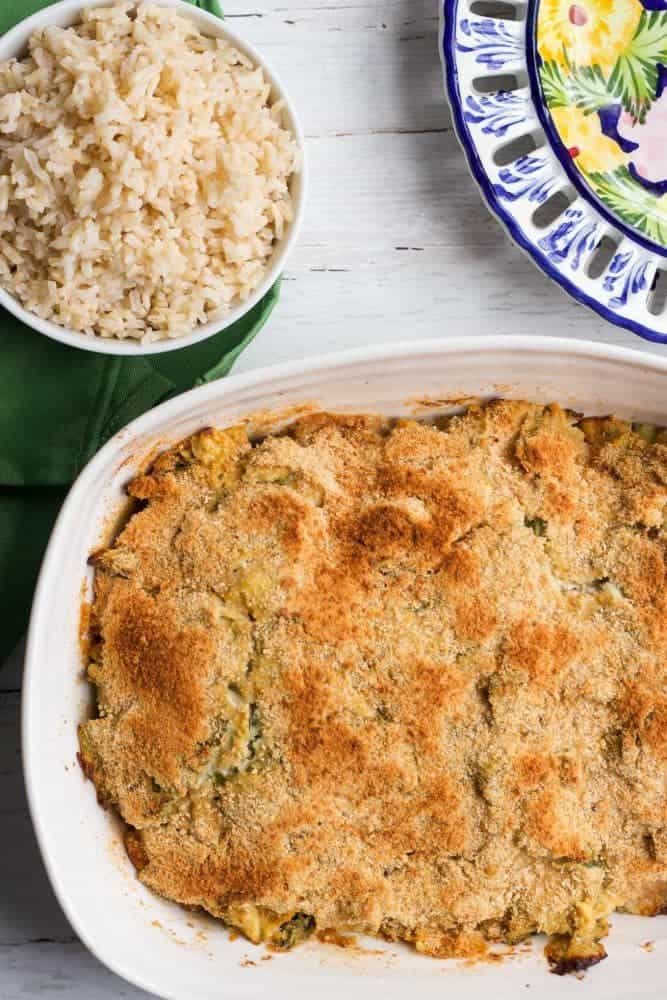 A baked casserole dish in a white pan with a golden brown topping a bowl of brown rice