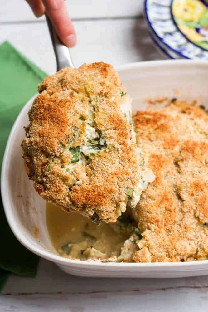 A crusted chicken breast being lifted from a casserole dish