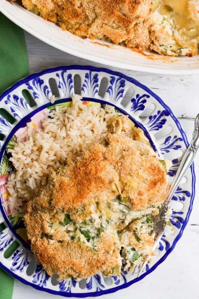 Creamy spinach artichoke baked chicken served on a blue and white plate over a bed of rice