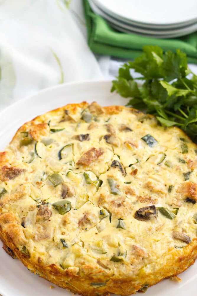 A baked vegetable egg frittata with a bunch of parsley decorating the serving plate