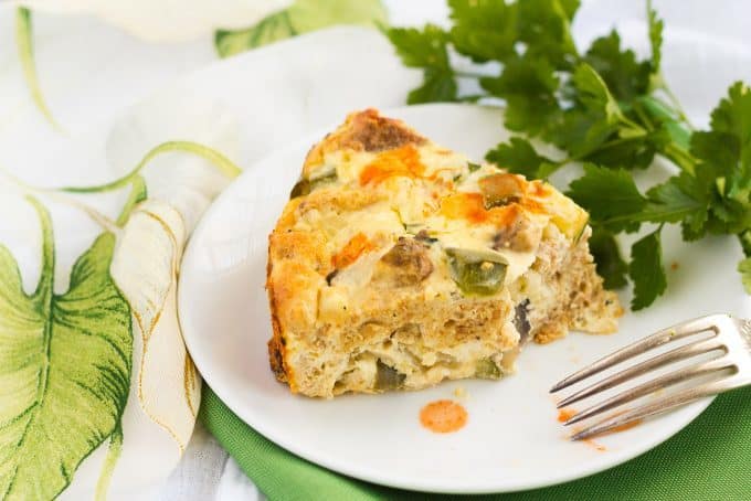 A slice of veggie egg frittata on a white plate with a bite taken out