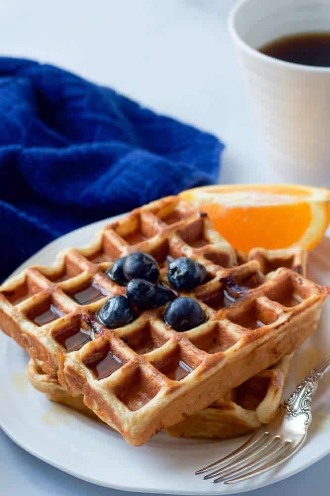 Two healthy blueberry waffles served on a plate with maple syrup and extra blueberries