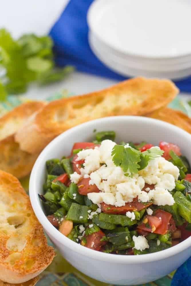 A bowl of mixed peppers with tomatoes and cheese and baguette slices nearby