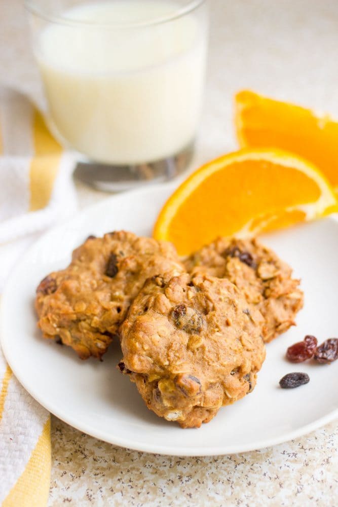 Healthy oatmeal raisin cookies served on a white plate with a glass of milk and some orange slices