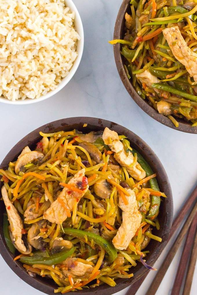 Two bowls of pork stir fry alongside a bowl of rice with chopsticks to the side.