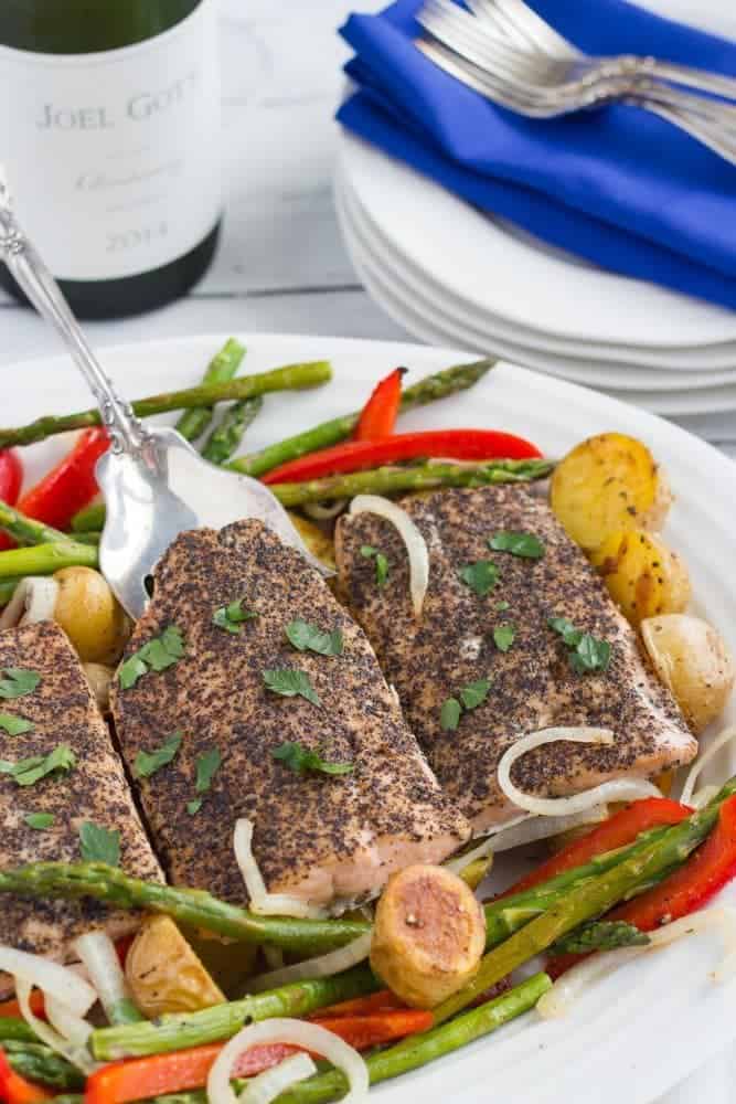 Peppered salmon being lifted from a platter where it's served over roasted vegetables