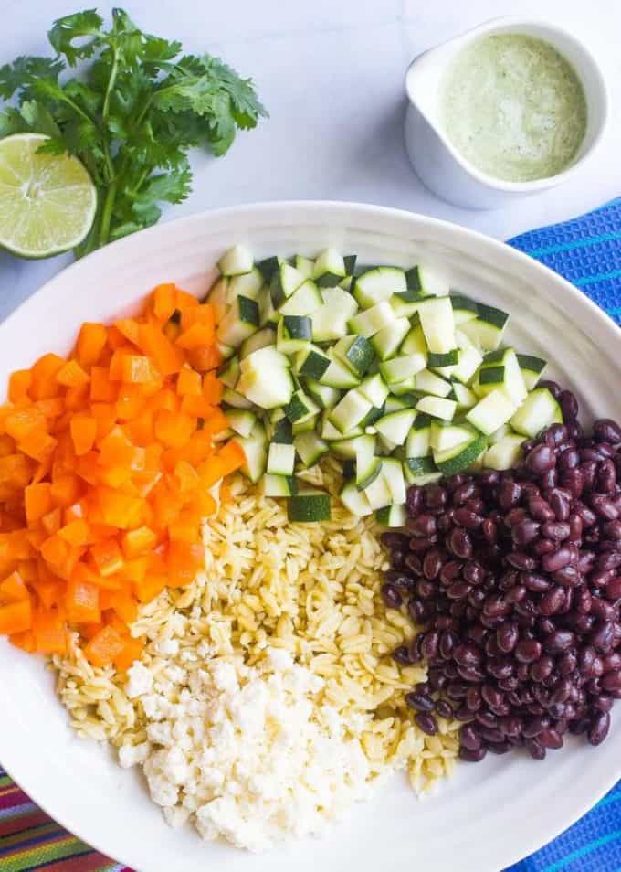 A large white bowl with orzo, zucchini, black beans, bell pepper and queso fresco in separate groups