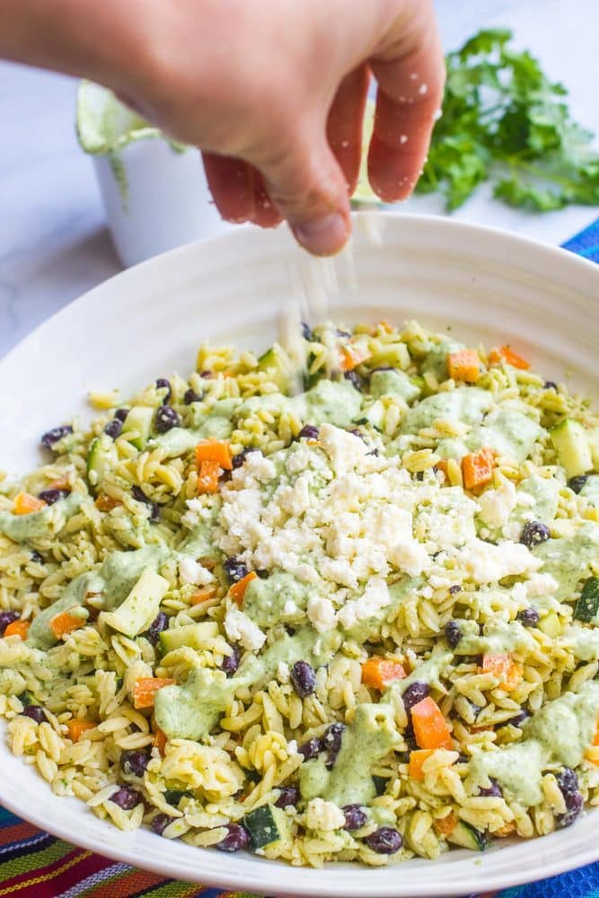 Crumbled queso fresco being sprinkled onto a southwestern pasta salad with black beans and zucchini