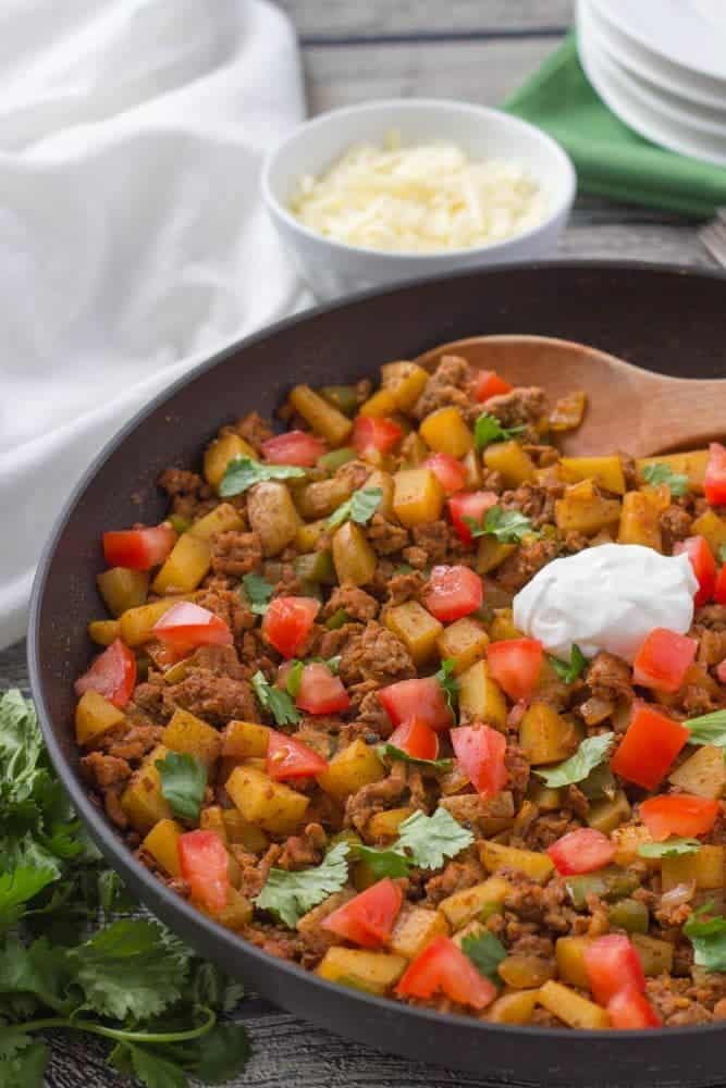 A skillet full of taco turkey mixed with diced potatoes and tomatoes plus cilantro and sour cream