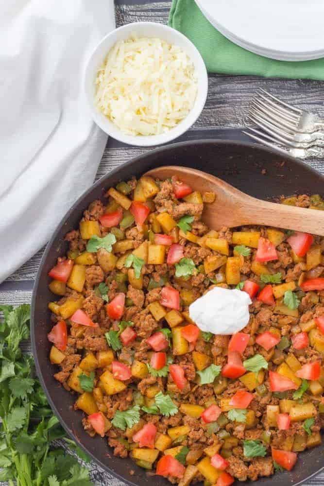 A skillet full of ground turkey potatoes, tomatoes and toppings