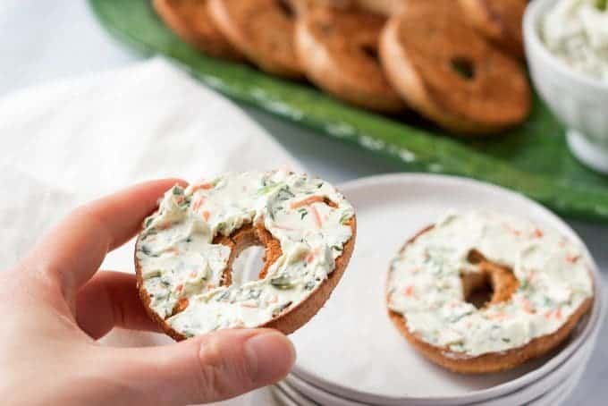 A hand picking up a toasted bagel half spread with cream cheese