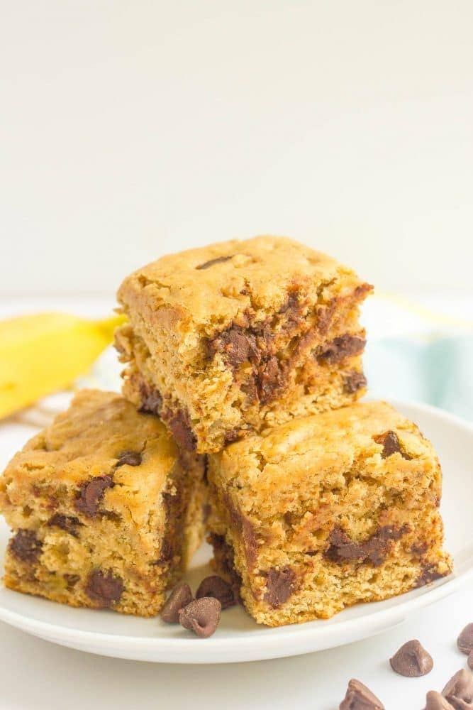 A stack of thick banana chocolate chip snack cake squares on a white plate