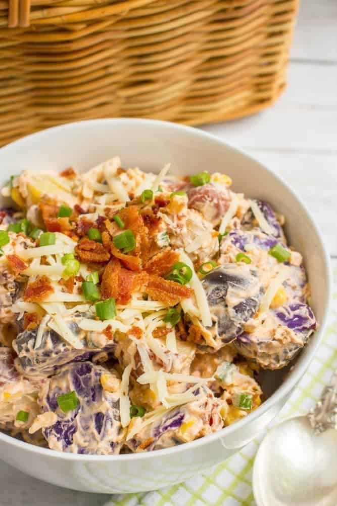 Serving bowl full of colorful potato salad with bacon and green onions on top