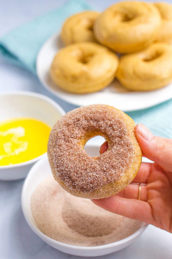 A hand holding up a donut that\'s just been dipped in butter and a cinnamon sugar mixture for coating.