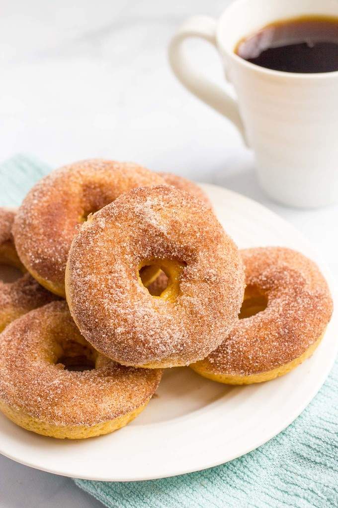 A plate with a pile of cinnamon sugar donuts with a cup of coffee to the side.