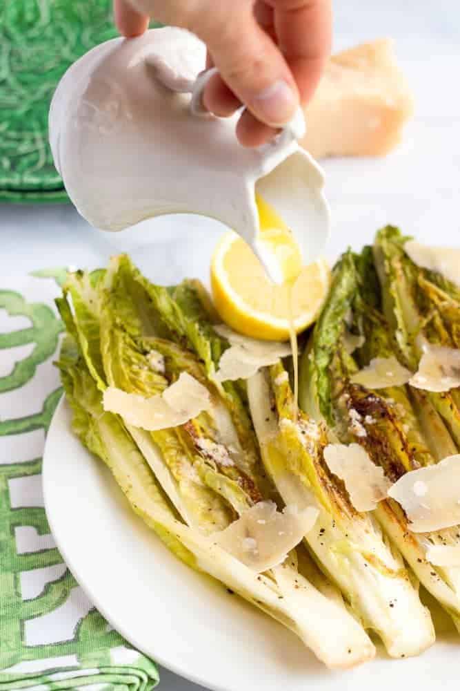 A small white pitcher pouring dressing over a grilled Caesar salad