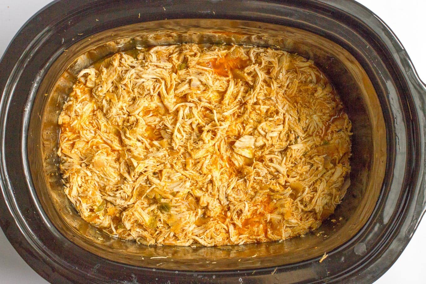 Shredded cooked tequila chicken in a slow cooker insert.