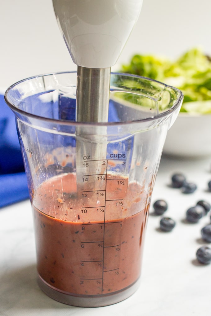 A blueberry balsamic vinaigrette being mixed up in a glass container using a stick blender