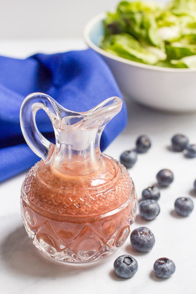 A blueberry vinaigrette in a small glass cruet with fresh blueberries to the side