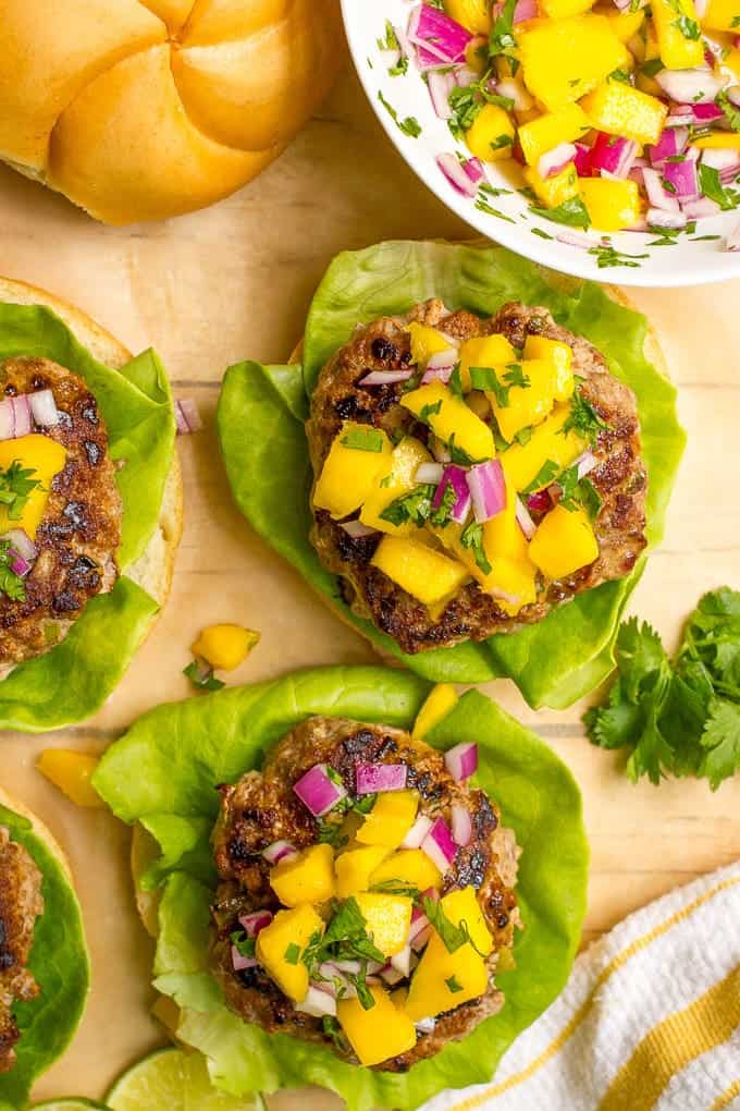 Pork burgers on buns with large leaf lettuce with a mango salsa on top.