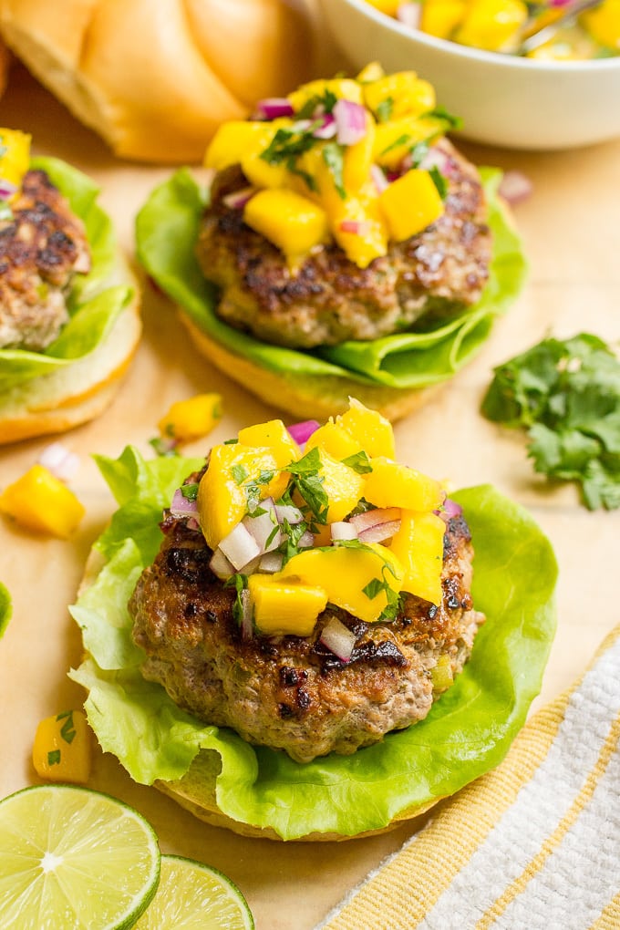 An open-faced burger on a bun topped with mango salsa with more burgers in the background