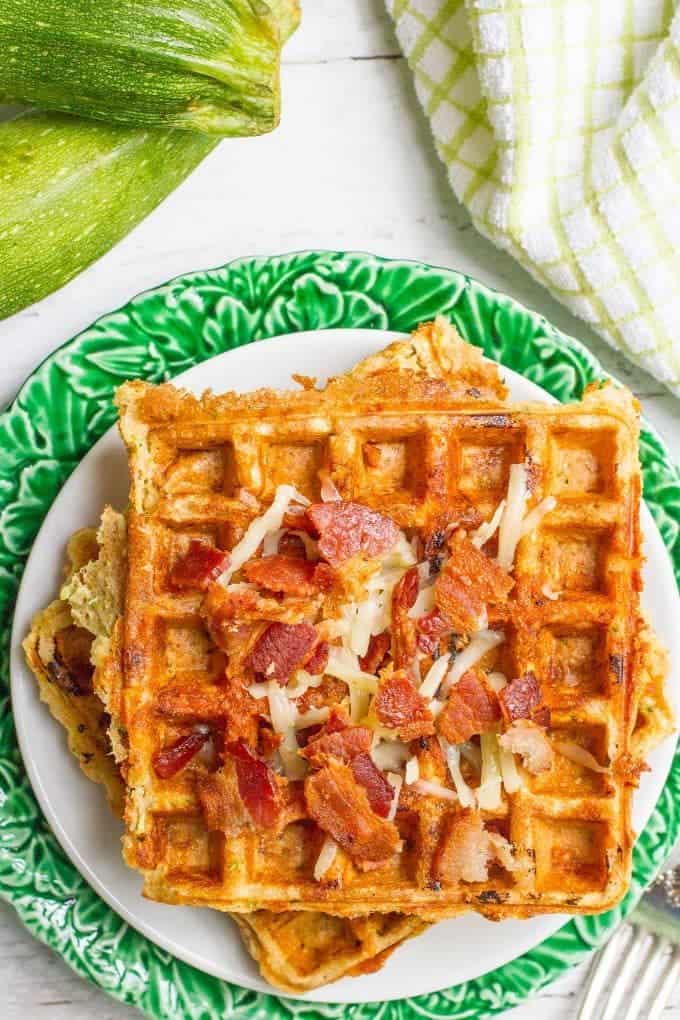 Savory zucchini waffles with cheese and bacon on top stacked and served on a white plate.