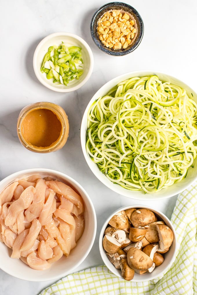 Ingredients for easy chicken satay with zucchini noodles, mushrooms and peanut sauce laid out in bowls