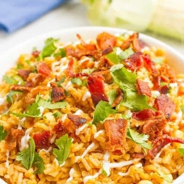 A large white bowl full of rice with bacon and corn topped with fresh parsley and a light drizzle of sour cream.