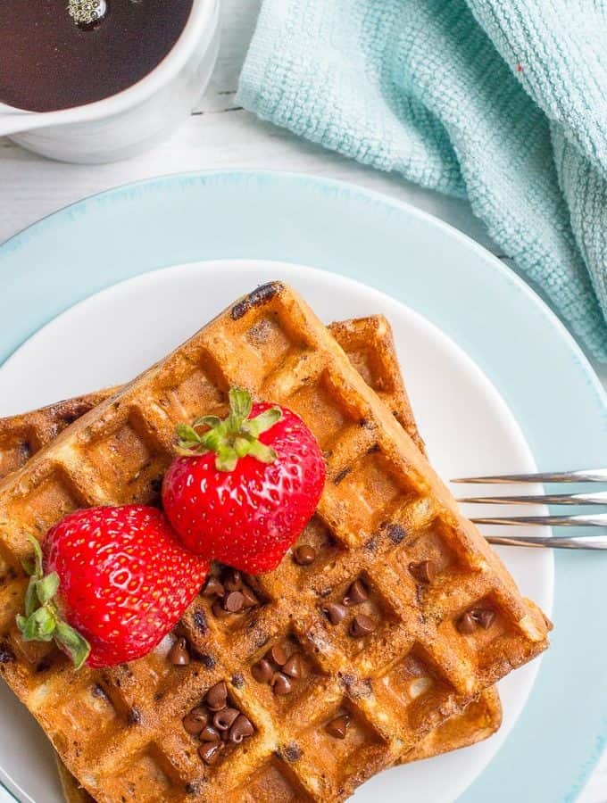 A fork resting on a plate of chocolate chip oatmeal waffle with fresh strawberries on top.