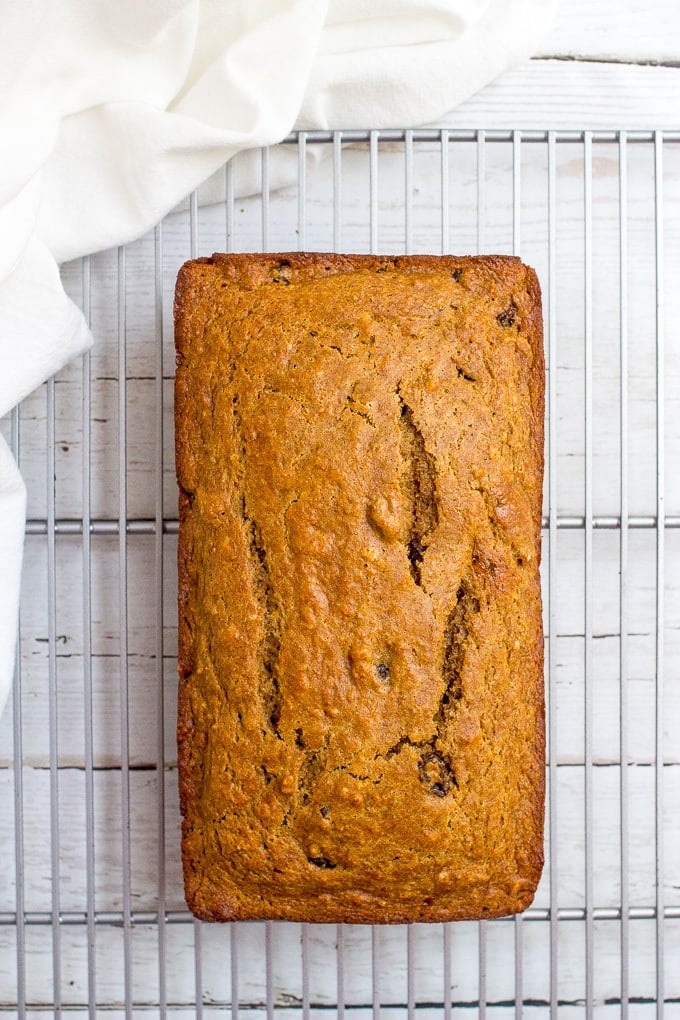 A golden brown loaf of a quick bread on a wire cooling rack.