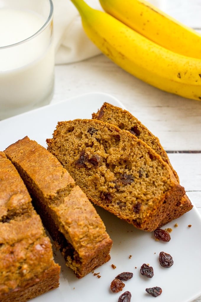 Cinnamon raisin bread slice don a white plate with bananas and a glass of milk in the background.