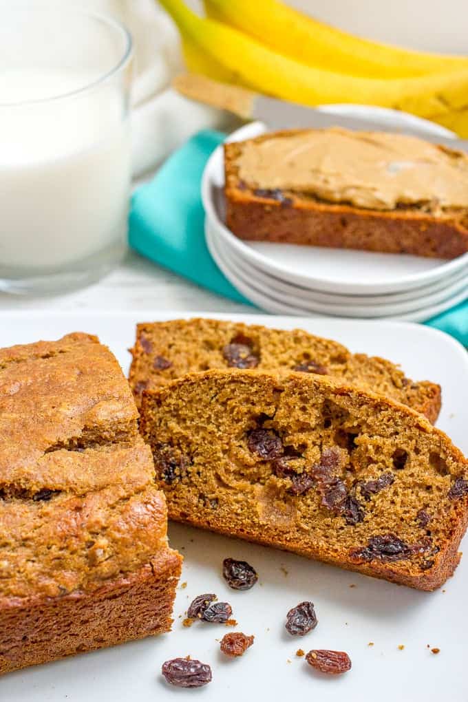 Close up of a sliced homemade cinnamon raisin bread on a white platter with a plate in the background with a slice topped with peanut butter.